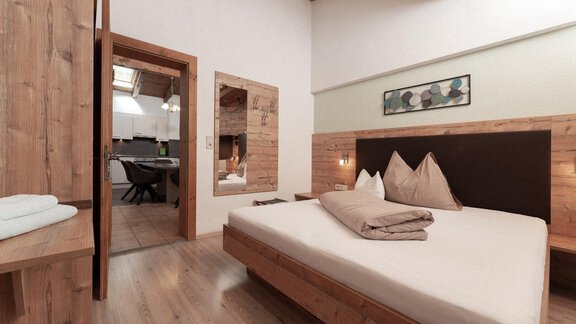 A modern bedroom with wooden furniture and a large bed. In the background, access to a combined living room and kitchen is visible. - Appartement Gehörde Sölden - Sölden