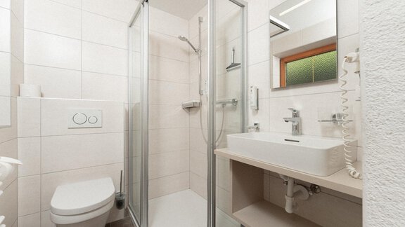 A modern bathroom with a shower and a sink. The walls are light-tiled and there is a window that lets in light. - Appartement Gehörde Sölden - Sölden