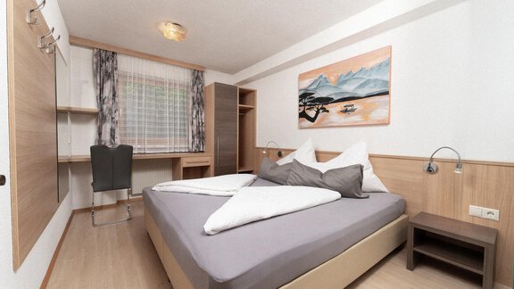 A modern bedroom with a large bed and bright wooden surfaces. A painting hangs on the wall, and there is a desk with a chair. - Appartement Gehörde Sölden - Sölden