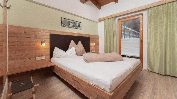 A cozy bedroom with a double bed and wooden paneling. Large windows and green curtains create a bright atmosphere. - Appartement Gehörde Sölden - Sölden