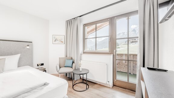 A modern bedroom with a large window and a cozy armchair. The bright decor creates an inviting atmosphere. - Appartement Montanara - Sölden