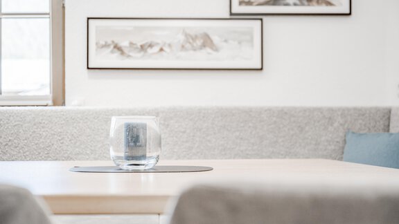A modern table with a glass vase is in the foreground. In the background, pictures on the wall and a cozy seating area are visible. - Appartement Montanara - Sölden