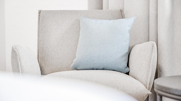 A cozy armchair with a light blue cushion. The background is kept light and simple. - Appartement Montanara - Sölden