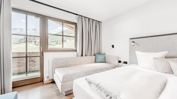 A modern bedroom with a large window and a comfortable bed. The furnishings are bright and friendly, with a cozy seating area. - Appartement Montanara - Sölden