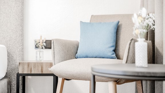 A modern chair with a blue cushion stands next to a small table. On the table, there is a flower vase with fresh flowers. - Appartement Montanara - Sölden