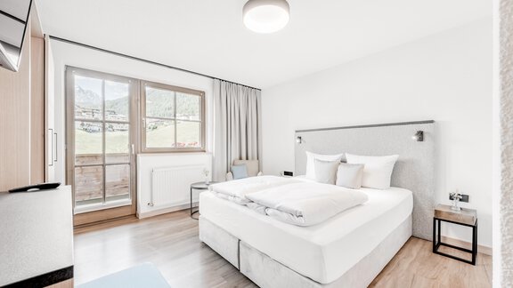 A modern bedroom with a large bed and light wooden floor. Large windows offer a view of nature outside. - Appartement Montanara - Sölden