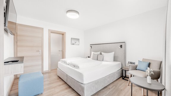 A modern bedroom with a large bed and bright walls. There is a small table and a chair as well as a television on the wall. - Appartement Montanara - Sölden