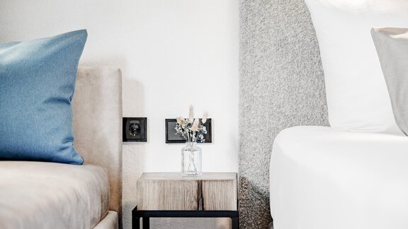 A modern bedroom with two beds. On the nightstand, there is a small vase with dried flowers. - Appartement Montanara - Sölden
