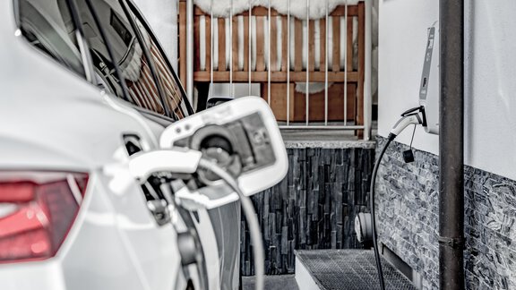 An electric car connected to a charging station. In the background, a bed is visible. - Appartementhaus Kathrin - Sölden