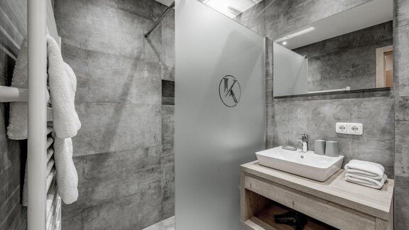 A modern bathroom with a shower and gray walls. On the shelf are towels and washing utensils. - Appartementhaus Kathrin - Sölden