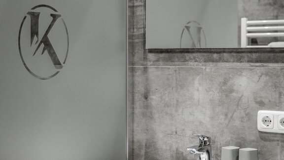 A modern bathroom with a clear sink and a mirror. The walls are made of gray concrete, and a frosted glass wall is visible. - Appartementhaus Kathrin - Sölden