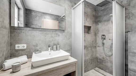 A modern bathroom with a shower and a sink. The walls are gray and there are large mirrors. - Appartementhaus Kathrin - Sölden