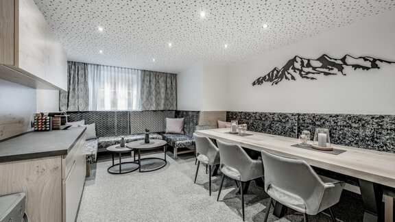 A modern living room with an elegant kitchen unit and a long dining table. The walls are painted in neutral colors, and the lighting creates a pleasant atmosphere. - Appartementhaus Kathrin - Sölden