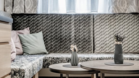 A modern living room with a comfortable, upholstered seating area and decorative cushions. On the coffee table, there are two vases with plants. - Appartementhaus Kathrin - Sölden