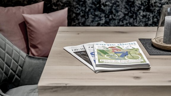A wooden table with magazines and a candle. In the background, there are upholstered cushions. - Appartementhaus Kathrin - Sölden