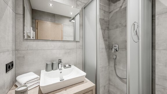 A modern bathroom with a shower and an elegant sink. The walls are bright and fitted with gray tiles. - Appartementhaus Kathrin - Sölden