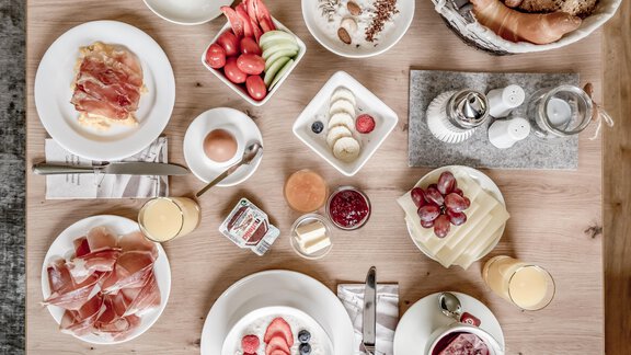 A hearty breakfast with various dishes on a table. There is fresh fruit, cold cuts, yogurt, and bread rolls. - Appartementhaus Kathrin - Sölden