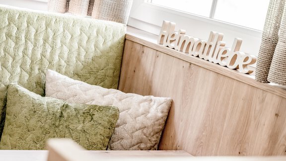 A cozy living area with green cushions and a wooden sign that says "Home Love." The room has plenty of natural light and an inviting atmosphere. - Appartementhaus Kathrin - Sölden