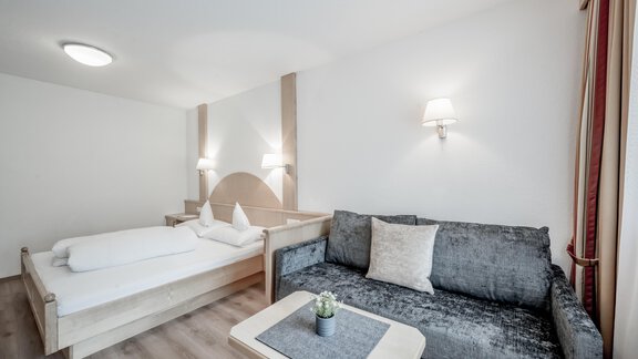 A modern bedroom with a single bed and a cozy sofa. The walls are painted light and there is soft lighting. - Appartementhaus Kathrin - Sölden