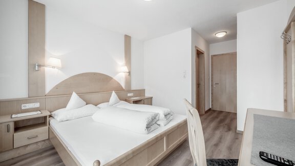 A bright and modern bedroom with a double bed and wooden details. The walls are in neutral tones, and there is a desk as well as appealing lighting. - Appartementhaus Kathrin - Sölden