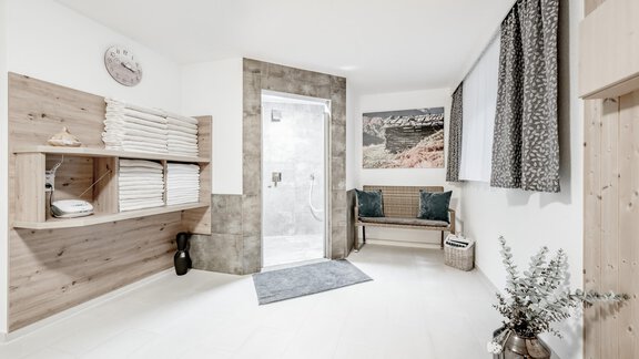 A modern wellness area with bright walls and wooden elements. In the background, a shower and a cozy seating area can be seen. - Appartementhaus Kathrin - Sölden
