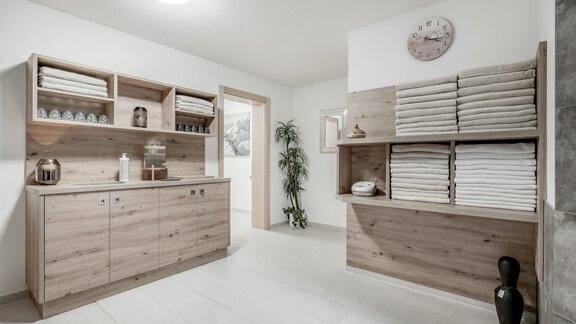 A bright, modern room with wooden shelves and neatly folded towels. A plant and a decorative clock complement the decor. - Appartementhaus Kathrin - Sölden