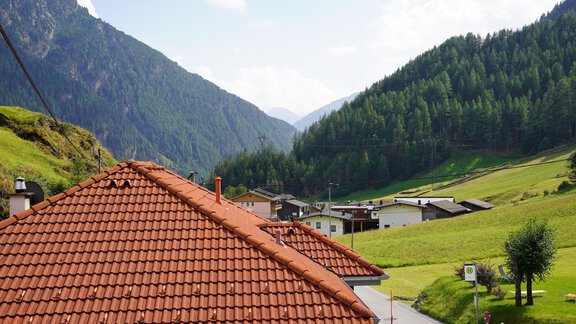 A picturesque landscape with green hills and mountains in the background. In the foreground, houses with red roofs can be seen. - Appt.  Bergheimat - Sölden