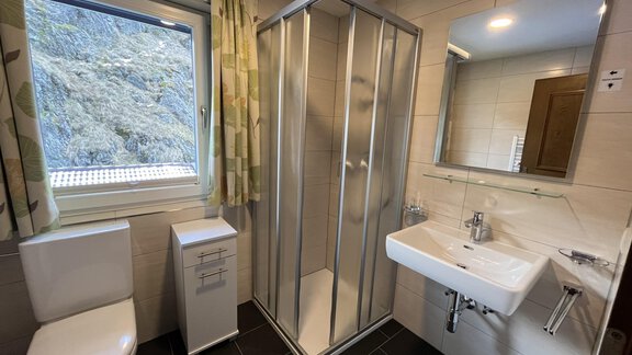 A modern bathroom with a shower, a sink, and a toilet. The room has a large window that lets in daylight. - Appt.  Bergheimat - Sölden
