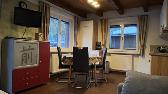 A cozy kitchen with a dining table, chairs, and a modern refrigerator. The walls feature windows and wooden paneling that create a warm atmosphere. - Appt.  Bergheimat - Sölden