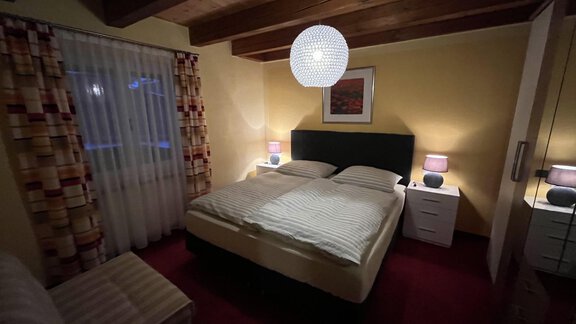 A cozy bedroom with a double bed and soft lighting. There is a small nightstand and an armchair, surrounded by warm colors. - Appt.  Bergheimat - Sölden