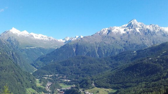 An impressive mountain landscape with snow-covered peaks and a green valley. In the background, small villages and lush forests can be seen. - Appt.  Ferienglück - Sölden