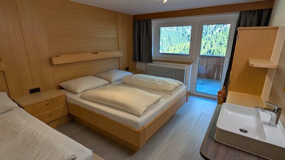 A modern bedroom with two beds, wooden furniture, and large windows. The room has a friendly atmosphere and a view of nature. - Appt. Rosmarie - Sölden