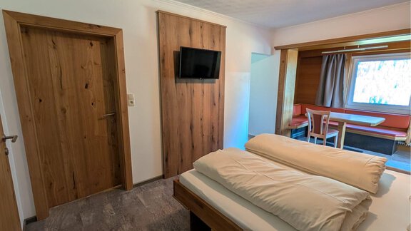 A cozy living room with wooden details and a large flat-screen TV. There is a double bed by the fully integrated living area and a small dining area. - Appt. Rosmarie - Sölden