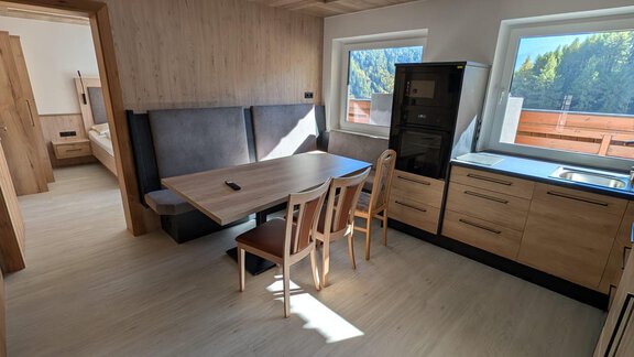 A modern dining room with a kitchen and a large dining table with wooden chairs. The large windows offer a view of the surroundings. The design is elegant and modern. - Appt. Rosmarie - Sölden