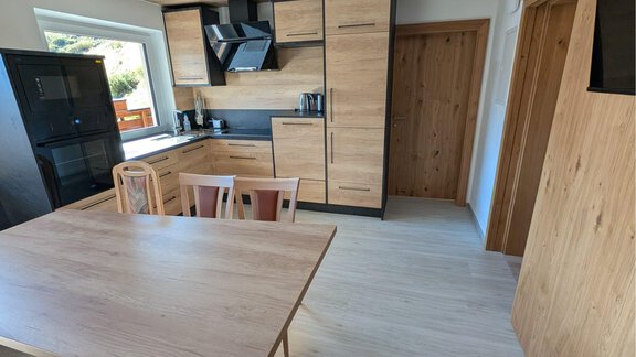 A modern kitchen with wooden cabinets, a large dining table, and a flat-screen TV. The room is bright and friendly with a large window. The decor is designed in a modern and elegant style. - Appt. Rosmarie - Sölden