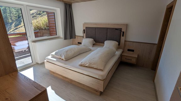 A modern bedroom with a large double bed and wooden details. Plenty of daylight pours in through the windows, creating a cozy atmosphere. - Appt. Rosmarie - Sölden