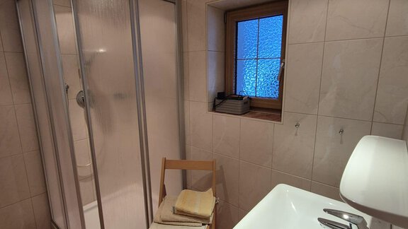 A modern bathroom with a shower and a sink. There is a chair and a window that lets in daylight. - Appt. Wildschütz - Sölden
