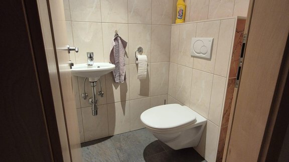 A modern bathroom with gray tiles and a white toilet. Towels hang on the wall and there is a small sink. - Appt. Wildschütz - Sölden