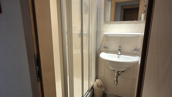 A small bathroom with a shower, a sink, and a mirror. The floor is equipped with tiles and a mat covering. - Appt. Wildschütz - Sölden