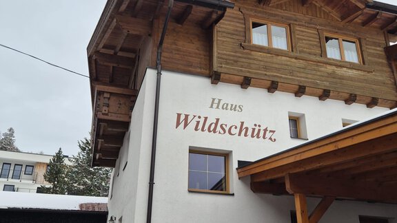 A cozy building with a wooden touch and the name "Haus Wildschütz" on the facade. The entrance area is covered, and some snow lies in the foreground. - Appt. Wildschütz - Sölden