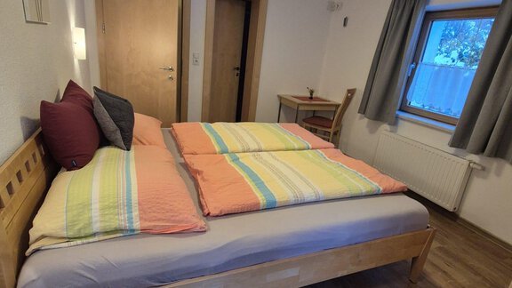 A bright bedroom with a large bed and colorful pillows. In the room, there is a table and a window with curtains. - Appt. Wildschütz - Sölden