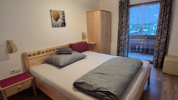 A cozy bedroom with a large bed and wooden furniture. The windows offer a view of a balcony with natural light. - Appt. Wildschütz - Sölden