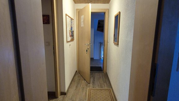 A bright hallway with wooden walls and a wood ceiling panel. At the end of the hallway, there is an open door leading to a room. - Appt. Wildschütz - Sölden