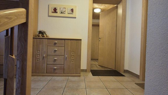A bright entrance area with tiled floor and wooden details. There is a chest of drawers and several doors leading to additional rooms. - Appt. Wildschütz - Sölden