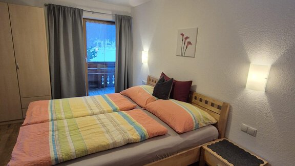 A cozy bedroom with a double bed and colorful bedding. The room has windows with curtains and is brightly lit. - Appt. Wildschütz - Sölden
