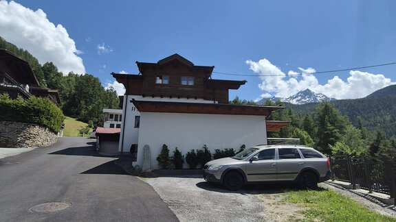 A modern house in the mountains with an asphalted path. In the foreground, there is a bright SUV, surrounded by green landscape. - Appt. Wildschütz - Sölden
