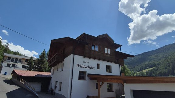 A typical alpine house with wooden cladding and a clear blue sky.  
Surrounded by a picturesque mountain landscape and green forests. - Appt. Wildschütz - Sölden