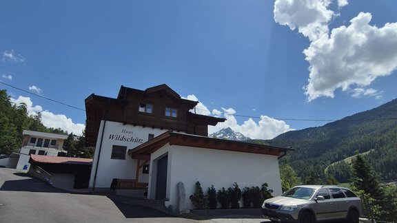 A modern building in a mountain landscape with a clear sky. In the foreground, a car is on the road. - Appt. Wildschütz - Sölden