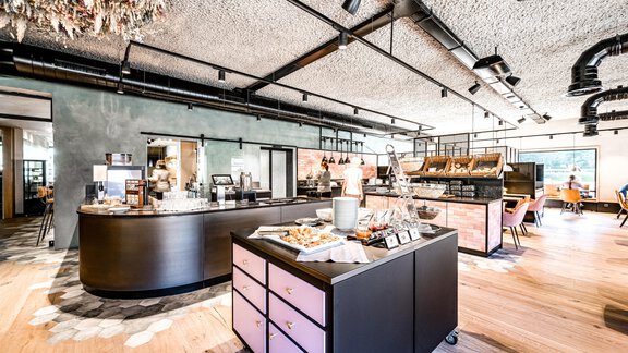 Ein modernes Café mit einer einladenden Theke aus Holz und verschiedenen Leckereien. Die Einrichtung ist hell und gemütlich, mit einem offenen Raumkonzept. - Bäckelar Wirt - Sölden