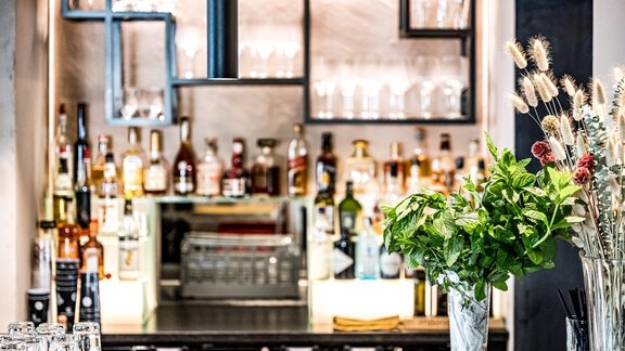 Eine stilvolle Bar mit einer Vielzahl von Spirituosen und Gläsern. Frische Blumen und dekorative Elemente verleihen dem Raum eine einladende Atmosphäre. - Bäckelar Wirt - Sölden